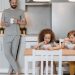 A father with two children enjoying breakfast in a bright, modern kitchen at home.