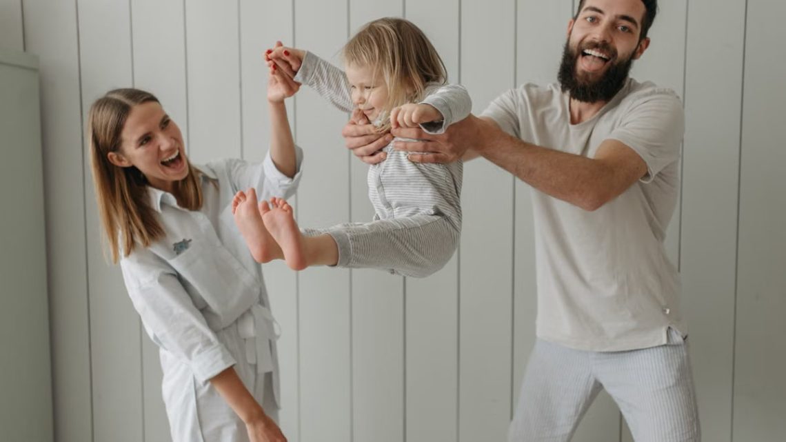 Joyful parents playing with their daughter indoors, all wearing white, capturing a moment of happiness.