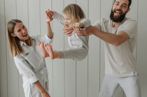 Joyful parents playing with their daughter indoors, all wearing white, capturing a moment of happiness.