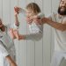 Joyful parents playing with their daughter indoors, all wearing white, capturing a moment of happiness.