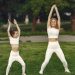Mother and daughter in matching activewear doing exercises outdoors on a sunny day.